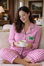 Woman in pink checkered pajamas with a green frog design, holding a cup of coffee on a couch.