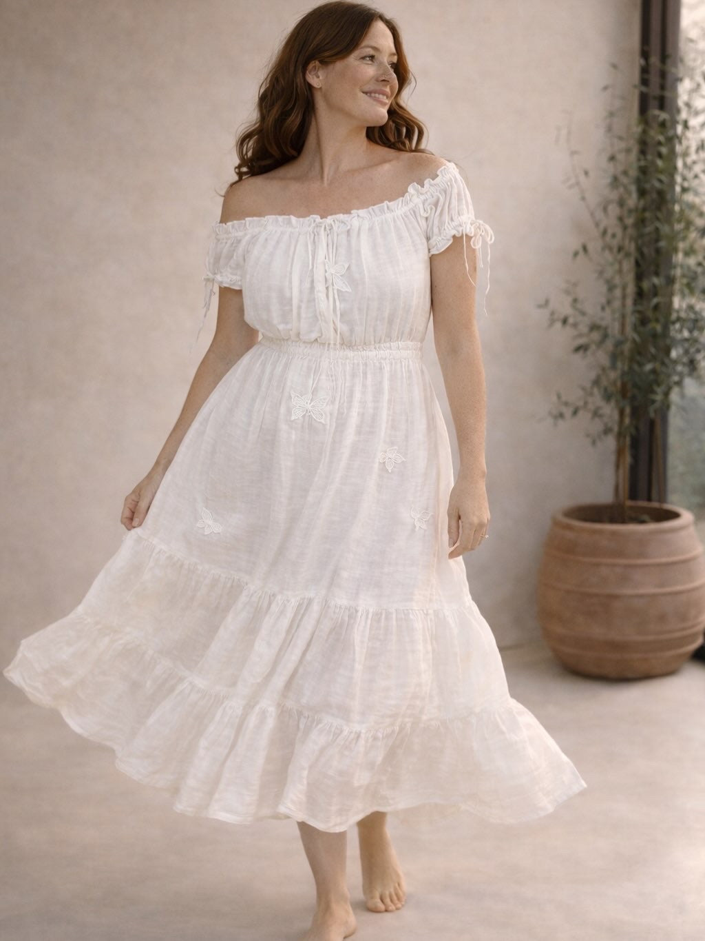 Woman wearing a white off-shoulder dress standing indoors with a neutral background