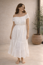 Woman wearing a white off-shoulder dress in a minimal indoor setting.